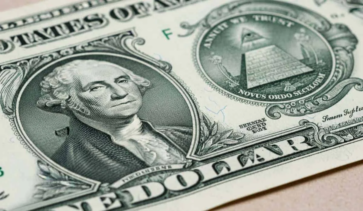 Billete de dólar estadounidense sobre una gráfica financiera que muestra la caída de la divisa en Colombia.