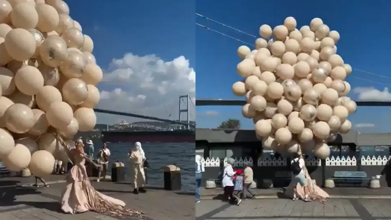 Novia con vestido rosa pálido sujetada por su fotógrafo ante un gran arreglo de globos empujado por el viento en Estambul