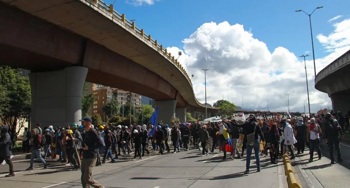 Manifestantes marchando por una vía principal de Bogotá afectando el tráfico y la operación de TransMilenio.