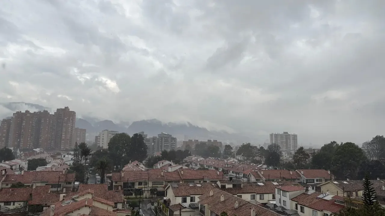 Vehículos transitando con precaución por una calle inundada en Bogotá durante una fuerte lluvia.