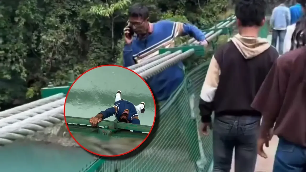 Hombre suspendido de sus brazos en la baranda de un puente sobre un río en un templo de India