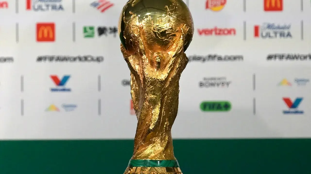 Balón de fútbol sobre el césped de un estadio con pantallas al fondo.